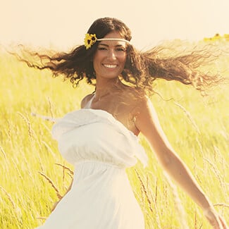 A woman wearing a floral wreath and sleeveless white dress spinning around in field of grass.