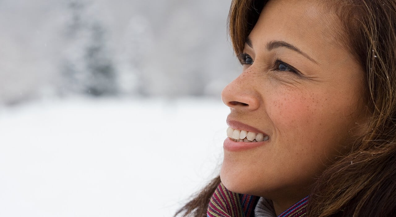 Older woman with brown hair looking upward and smiling  against snowy background.