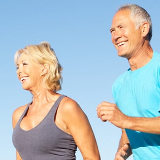 Older woman and man jogging on the beach and smiling