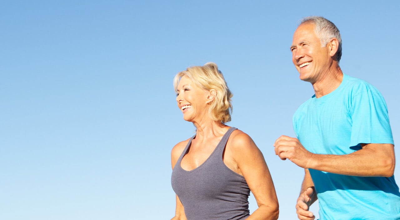 Older woman and man jogging on the beach and smiling.