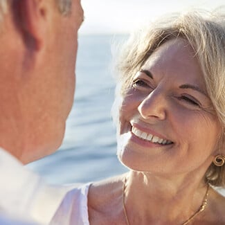 Older woman with smooth skin smiling at her husband on the beach.