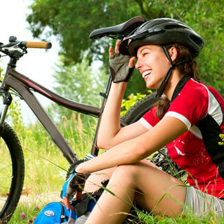 Woman wearing bike helmet and cycling clothing sitting besider her bike at the park.