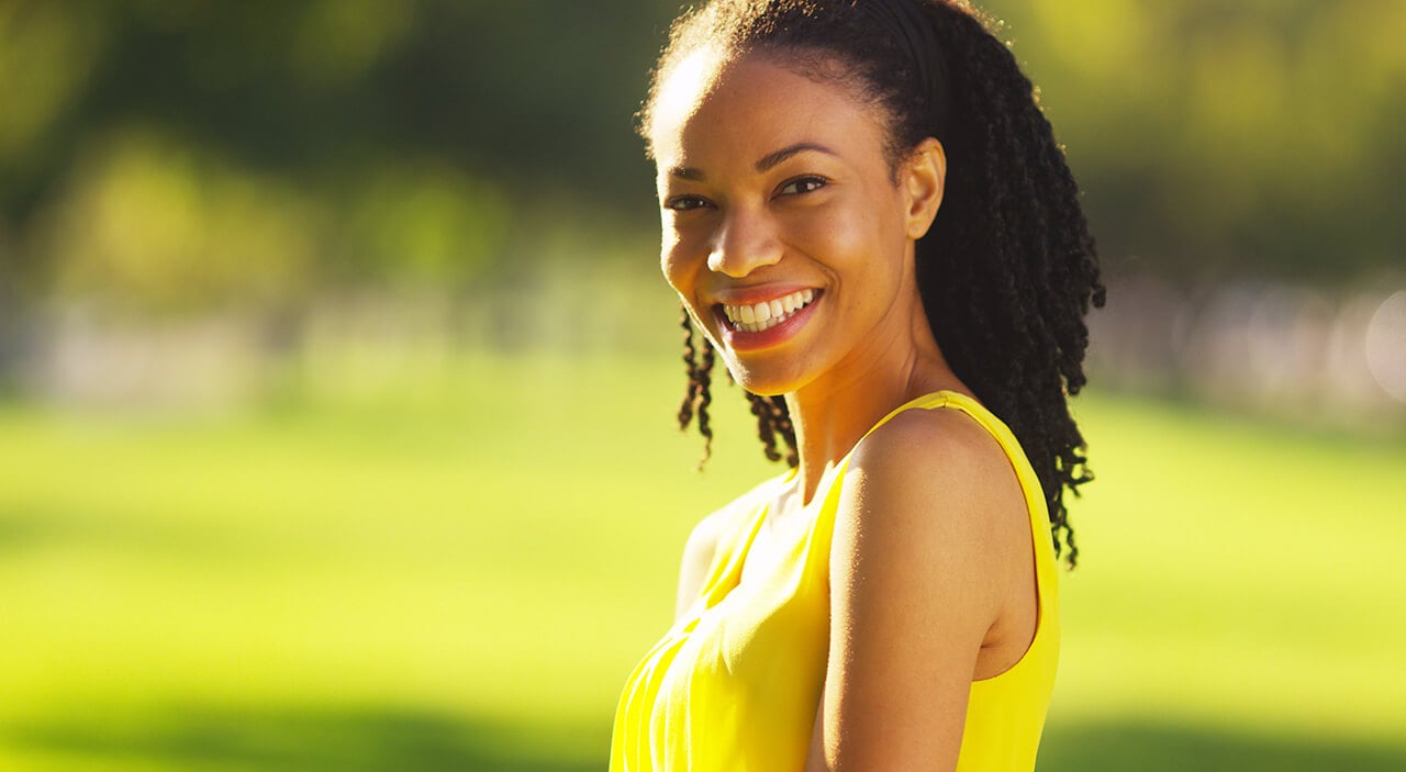 Woman wearing yellow dress smiling in park during summer.