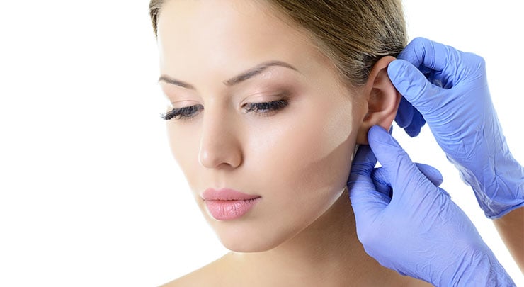 Woman having her ear inspected by a doctor wearing blue rubber gloves.