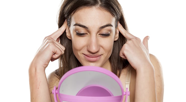 Woman looking at mirror while pushing back her prominent ears.