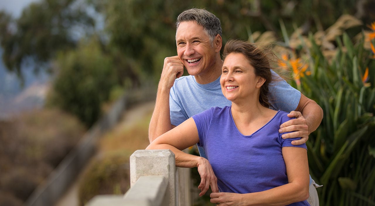 Older woman and man smiling and looking out at the water while wind blows through their hair.