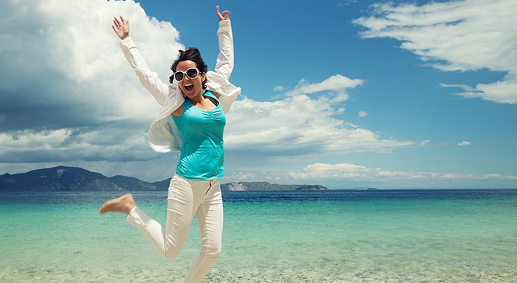 Woman jumping on beach happy after breast reduction.