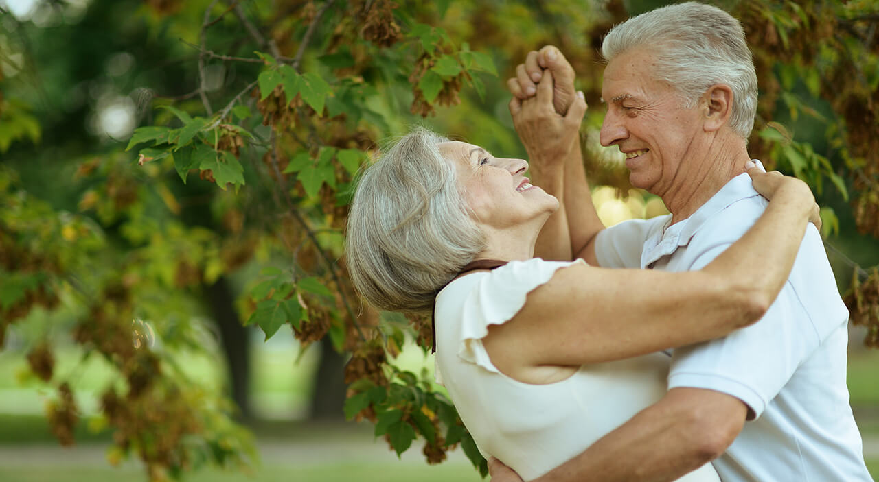 Older woman smiling up at her husband as they dance together in the park.
