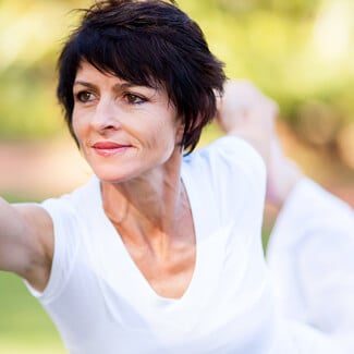 Older woman holding a yoga pose with one arm stretched out in front of her and the other holding on to her leg behind her.