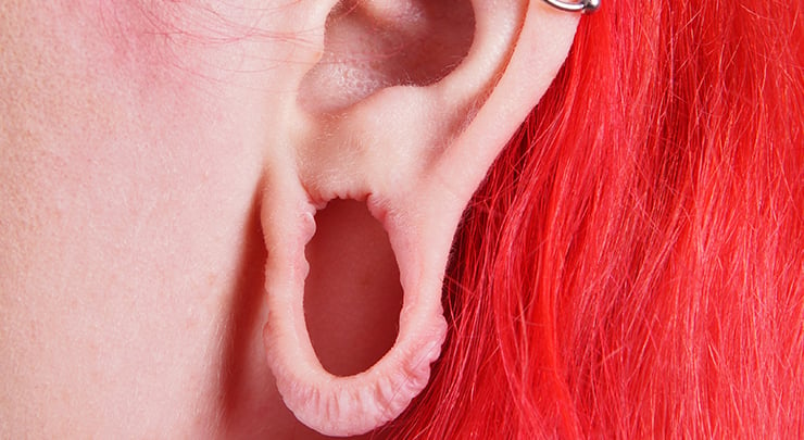 Woman's ear with dangling huge earlobe from gauge.