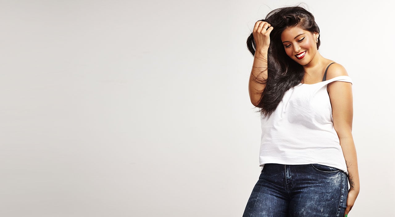 Full figured woman smiling and wearing tight jeans and white tank top.