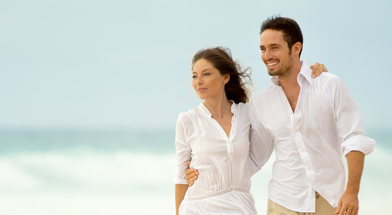 Woman and man looking out to the water as they walk on the beach. 