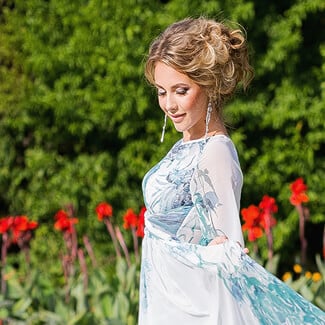 Woman wearing blue dress with hair upswept in bun as she walks through a garden with pretty flowers.