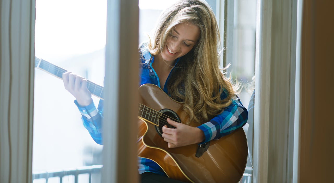 Woman sitting at window playing guitar and smiling.