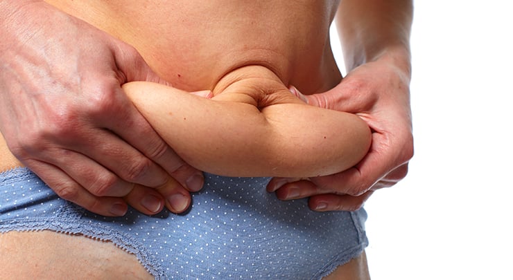 Woman pinching her loose skin and fat on her stomach.