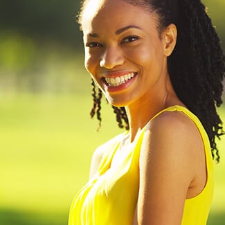 Woman smiling over her shoulder and wearing yellow dress at the park.