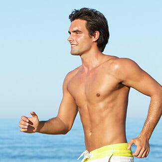 A man wearing swimming trunks running on the beach.