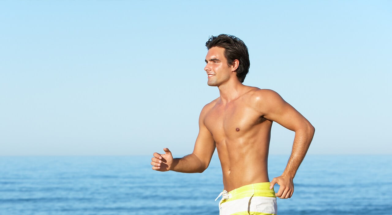 Man in swimming trunks running on beach in the sun.