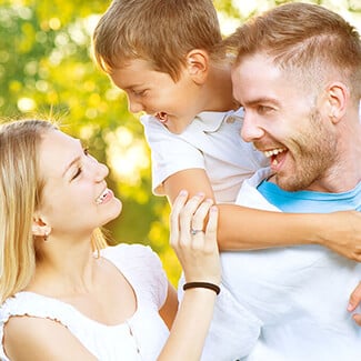 Blonde mother looking up at son on father's back while they're all smiling in the park.