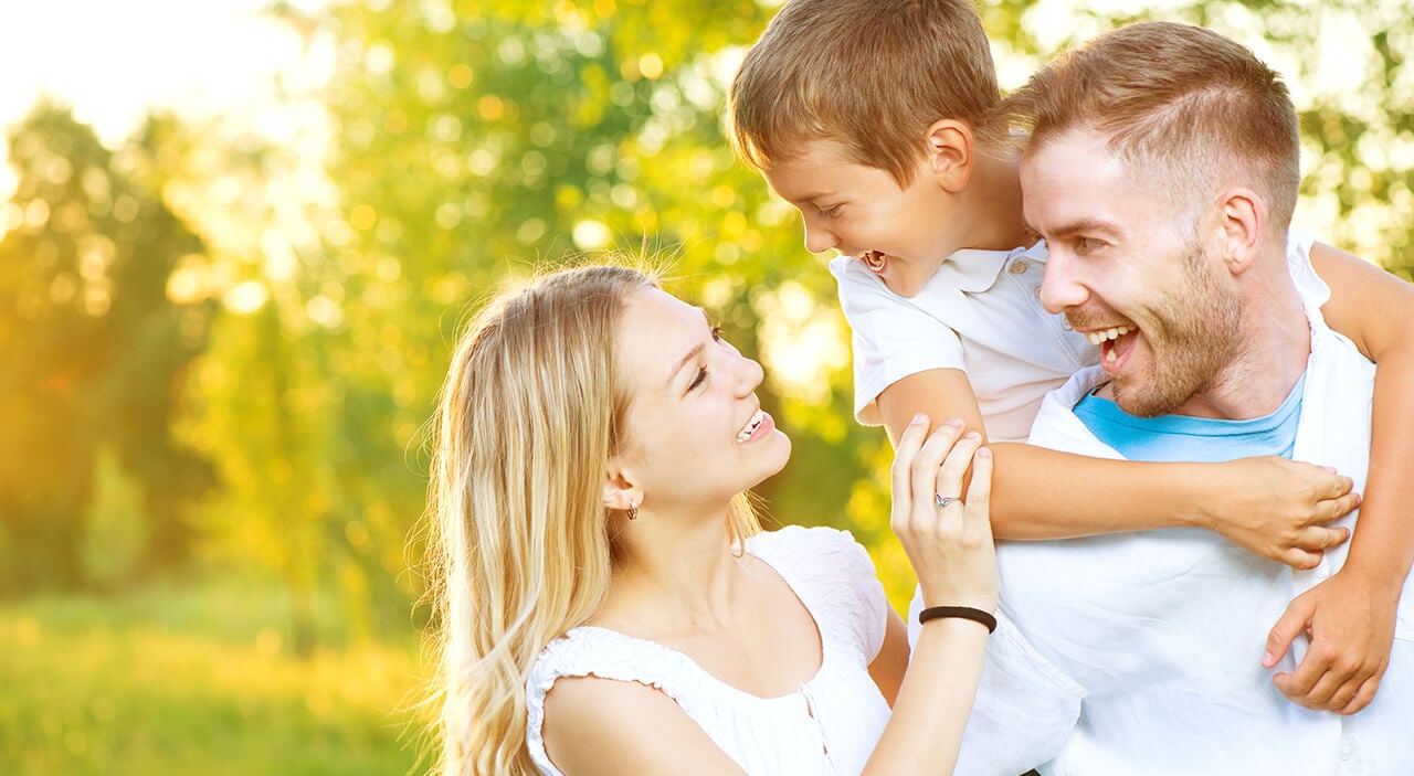 Mother looking up at son on father's back and smiling in the park.