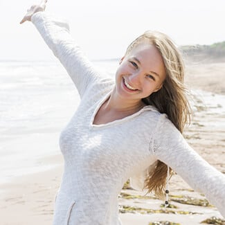 Woman wearing white shirt at the beach with hands outstretched and smiling.
