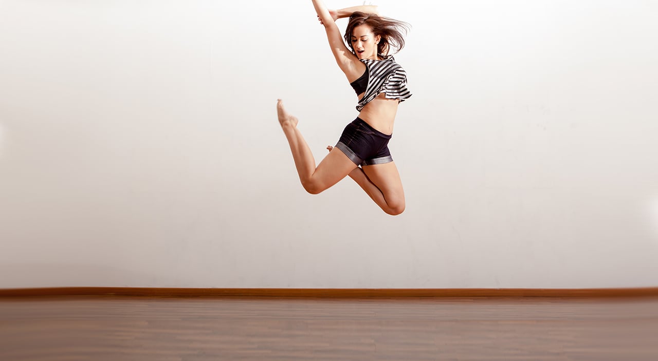 Young woman wearing a striped shirt and shorts jumping up in mid air while dancing.