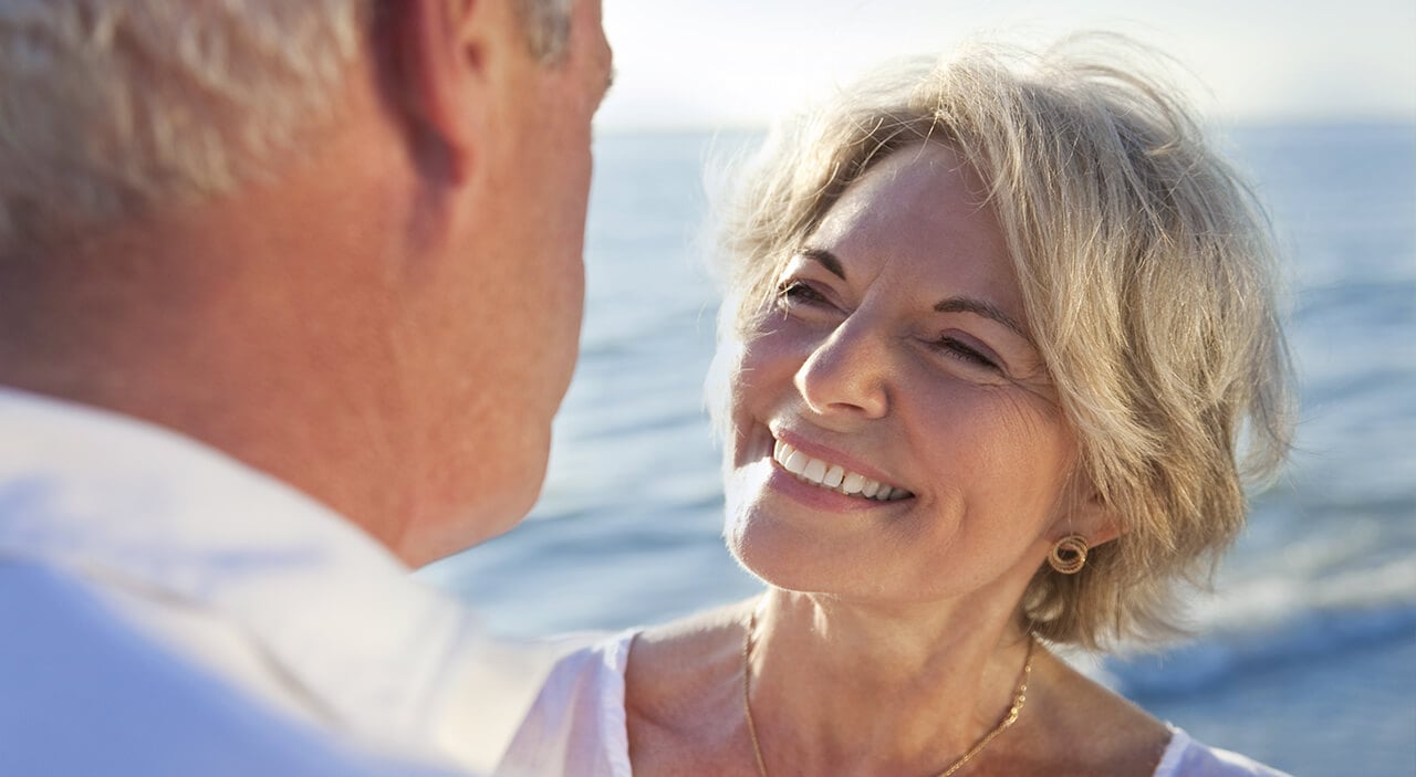 Older blonde woman smiling up at her husband at the beach.