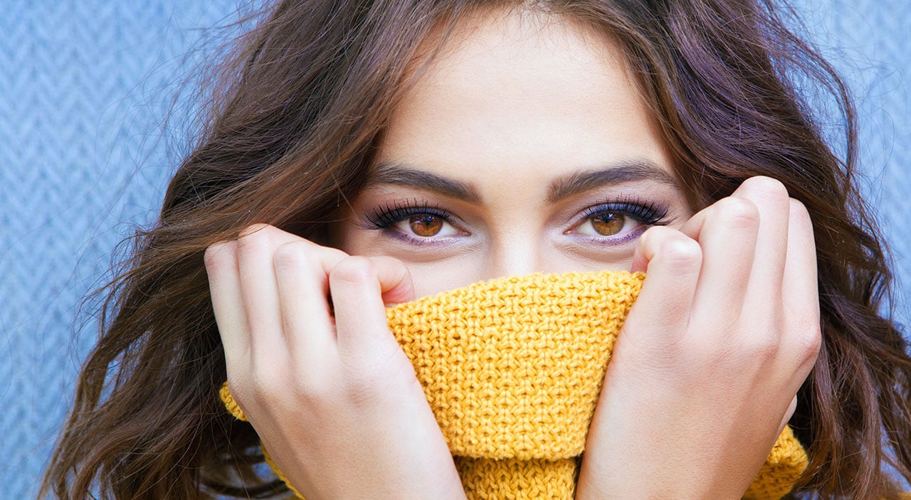 Young woman with brown hair covering her face except her brown eyes with a yellow sweater.